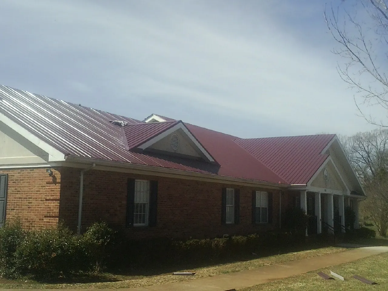 Red metal roof with gabled entries on a long brick building, from a Hail Damage Roof Repair job in Missoula