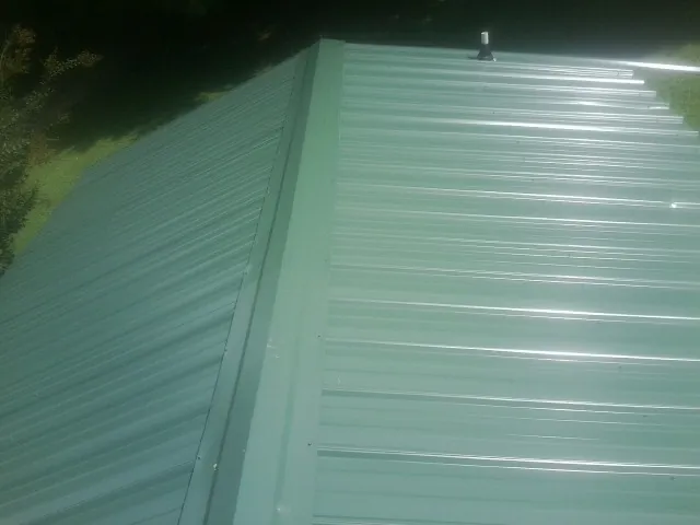 New green metal panels meeting at the ridge of a roof — Flat Roof Repair work by our crew in Missoula