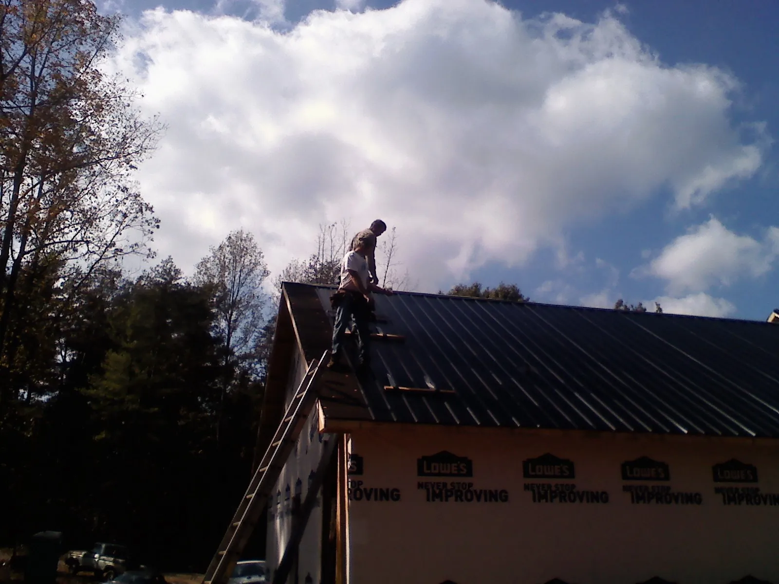 Roofer fastening dark metal panels high against a cloudy sky, from a Roof Inspection job in Missoula