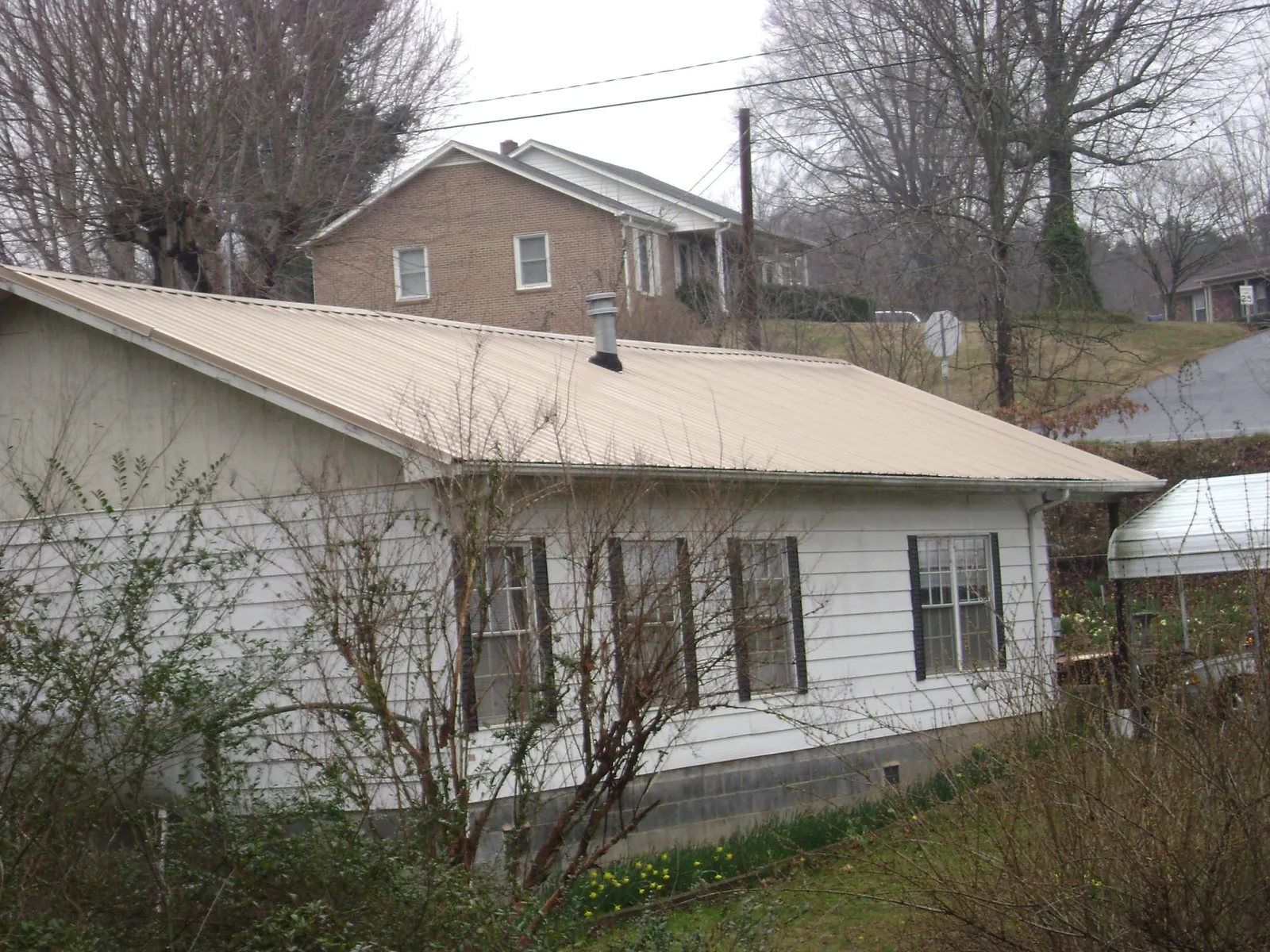 Tan metal roof on a white sided house set into a hillside — Commercial Roofing by Roofing Brothers in Missoula